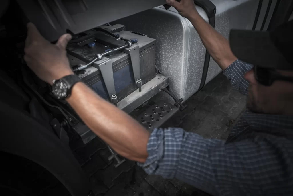 Technician performing a truck battery replacement with safety precautions.