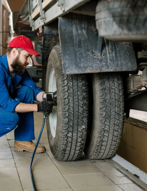 A bearded mechanic checking the tires pressure of a truck.