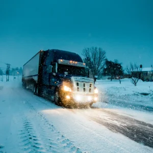 Truck driving through snow, highlighting cold weather conditions that increase the need for jumpstarts.
