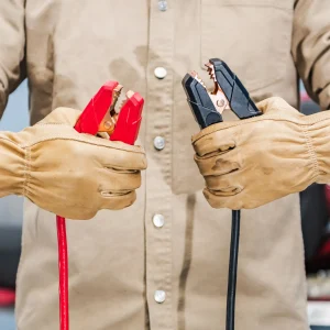 Mechanic holding red and black jumper cables, essential tools for performing jumpstarts on vehicles with dead batteries.