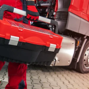Technician with toolbox ready for truck battery replacement service.